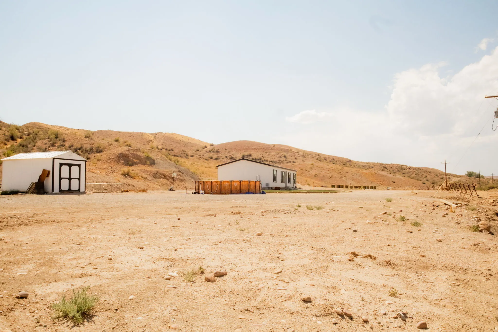 Expansive undeveloped land featuring a detached shed, a single-story residence with white siding, and a fenced outdoor area