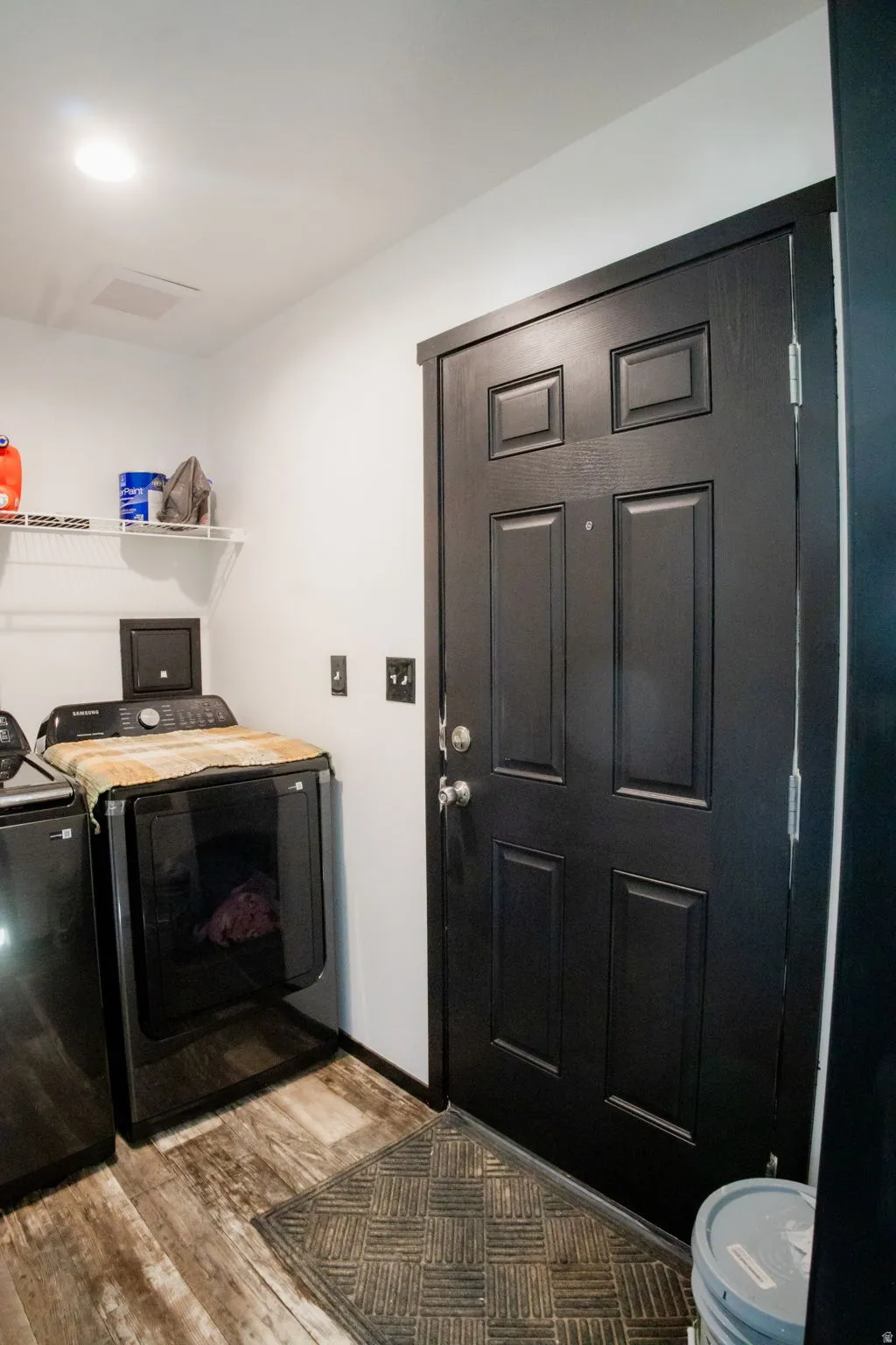 Utility area featuring wood-finish flooring and a black paneled door with coordinating trim
