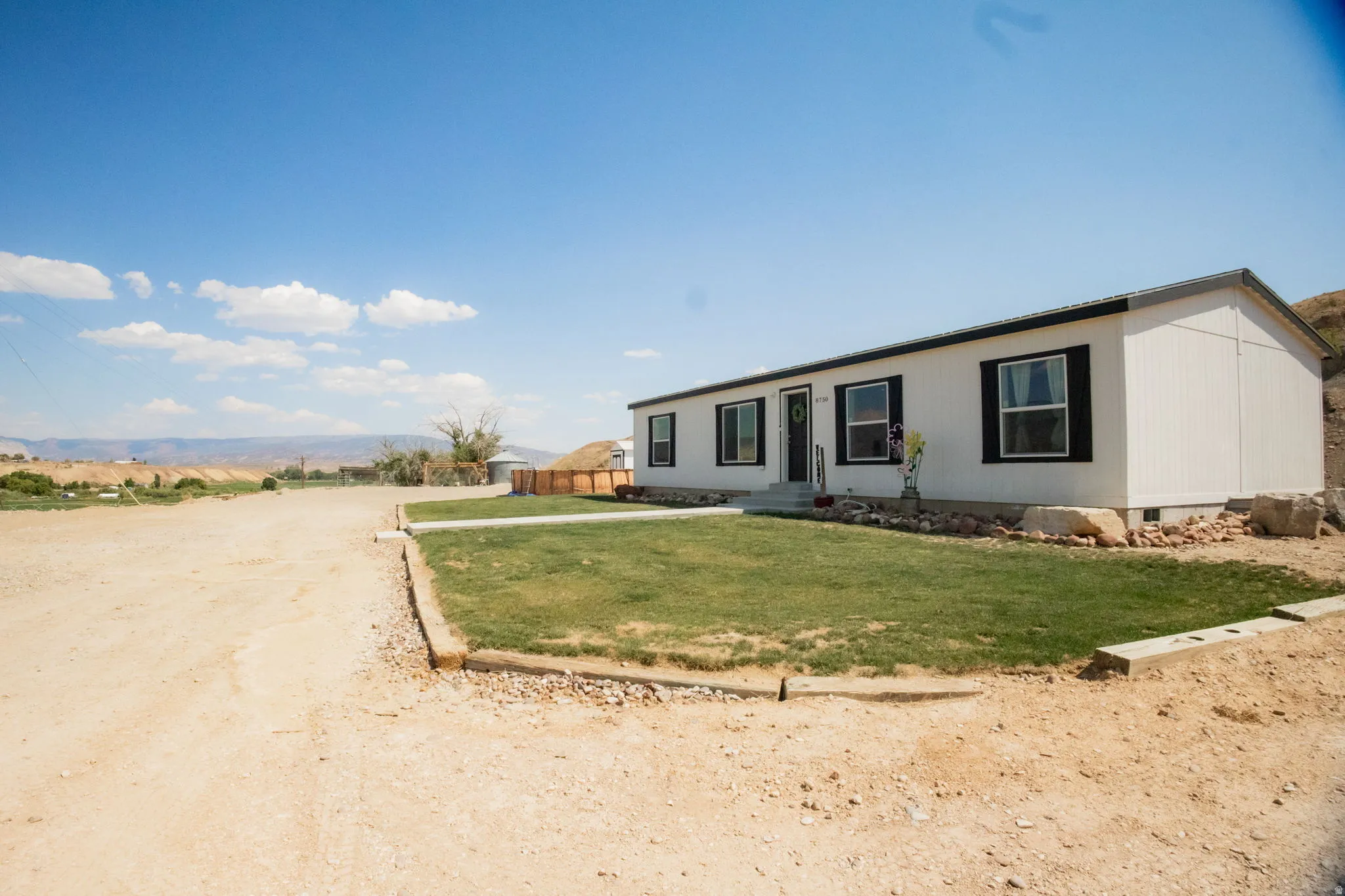 White exterior with black window trim and shutters, green lawn, gravel driveway, and a distant mountain backdrop