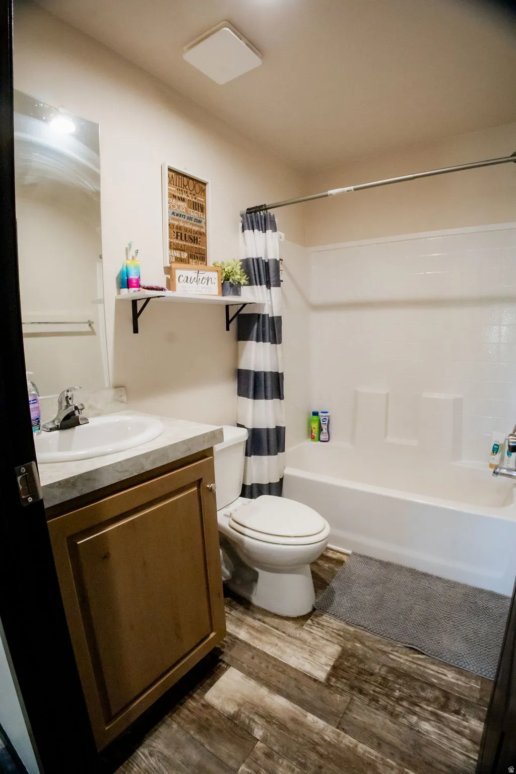 Bathroom featuring a white tub and shower combination, wood-finish flooring, a single vanity with a light-toned countertop, and built-in shelving