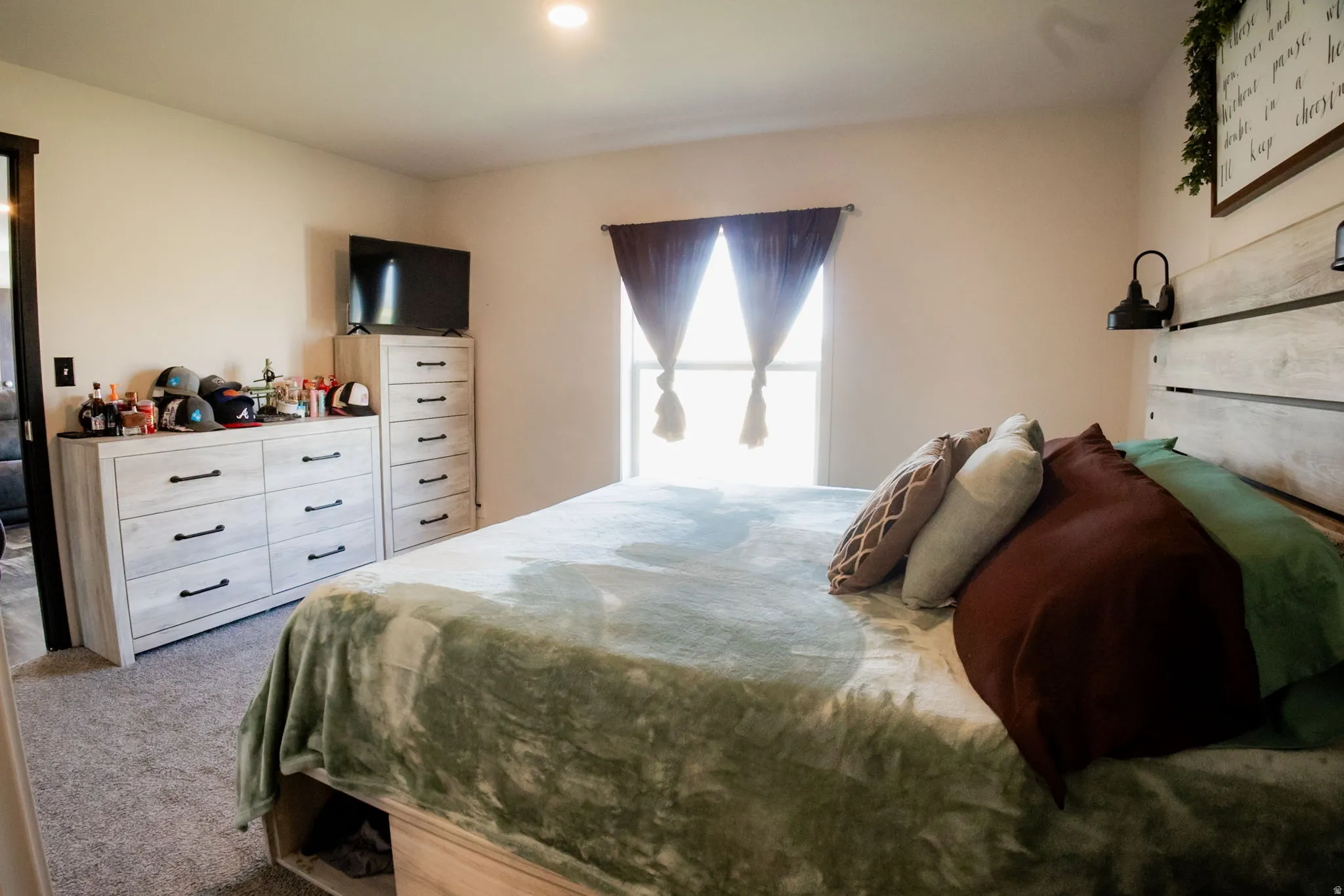 Carpeted bedroom featuring a window with dark curtains, a light-toned wooden headboard, and recessed ceiling lighting