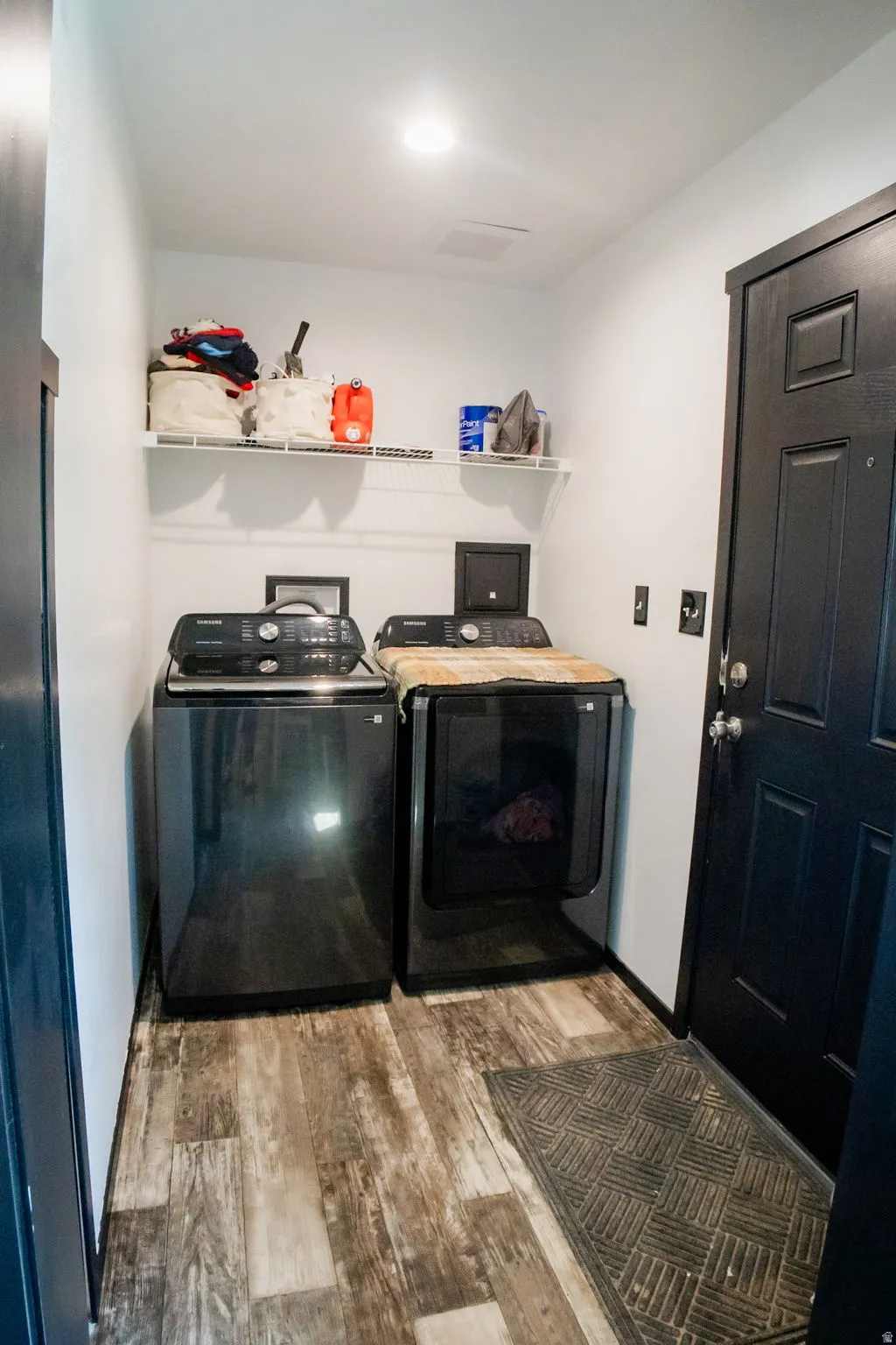 Dedicated laundry space featuring wood-finish flooring, white walls, and a black paneled door