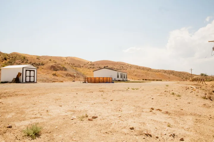 Expansive undeveloped land featuring a detached shed, a single-story residence with white siding, and a fenced outdoor area