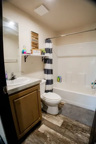 Bathroom featuring a white tub and shower combination, wood-finish flooring, a single vanity with a light-toned countertop, and built-in shelving