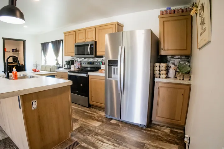 Kitchen featuring wood-finish flooring, stainless steel appliances, light wood-tone cabinetry, light-toned countertops, and a tiled backsplash