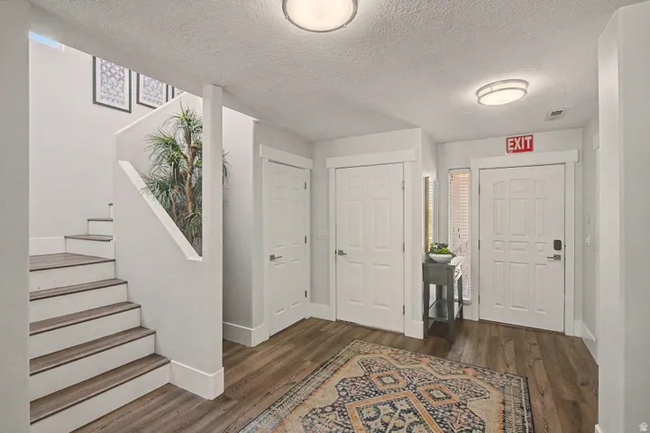 Entryway featuring wood-finish flooring, a contemporary staircase with white risers, multiple panel doors with white trim, and flush-mount lighting fixtures
