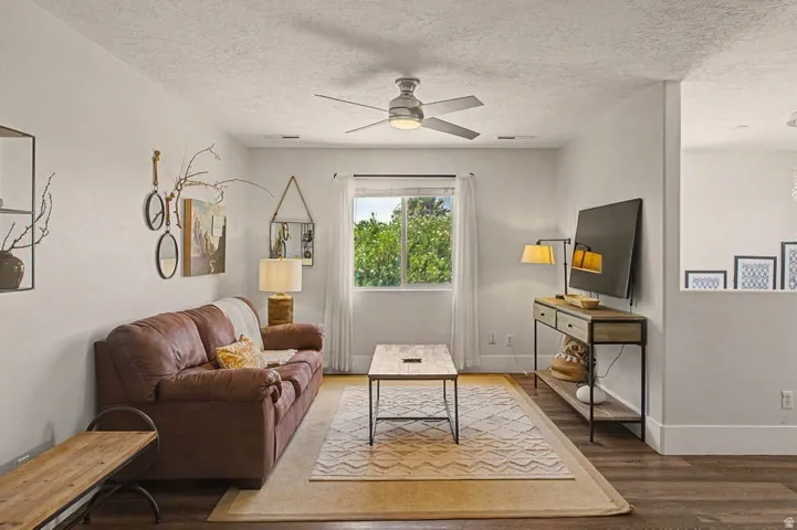 Living area featuring wood-finish flooring, a ceiling fan with light fixture, a window with exterior views, and a half-height wall
