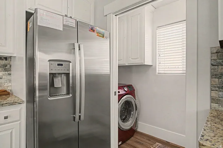 Stainless steel side-by-side refrigerator with an integrated ice and water dispenser, framed by white cabinetry and a mosaic tile backsplash