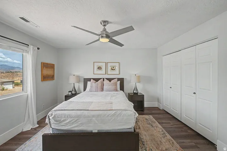 Room featuring wood-finish flooring, a ceiling fan with integrated lighting, a window with exterior scenery, and bi-fold closet doors