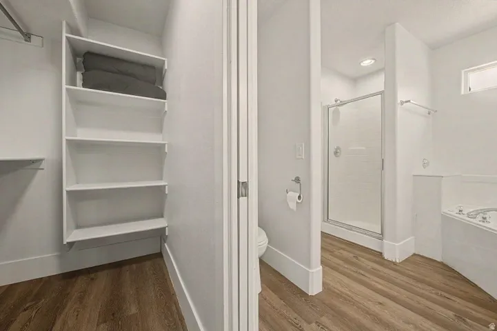 Bathroom featuring wood-finish flooring, a glass-enclosed shower, built-in soaking tub, recessed lighting, and a closet with shelving