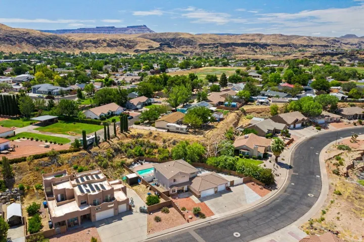 Curved street lined with single-story and multi-story homes, featuring mature green trees and desert landscaping