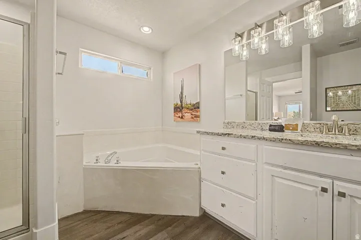 Bathroom featuring a built-in jetted tub, wood-finish flooring, white vanity with a light-colored speckled countertop, and a glass-enclosed shower