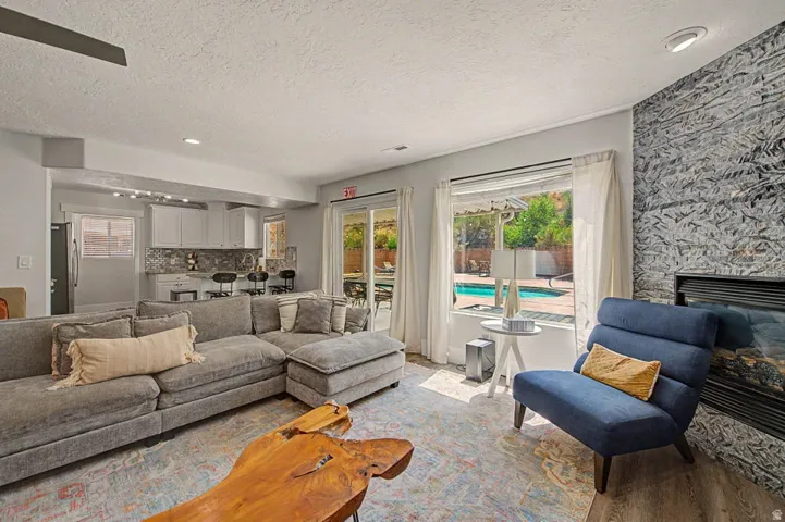 Spacious living area featuring a fireplace with a textured stone surround, wood-finish flooring, and a large sliding glass door opening to an outdoor pool