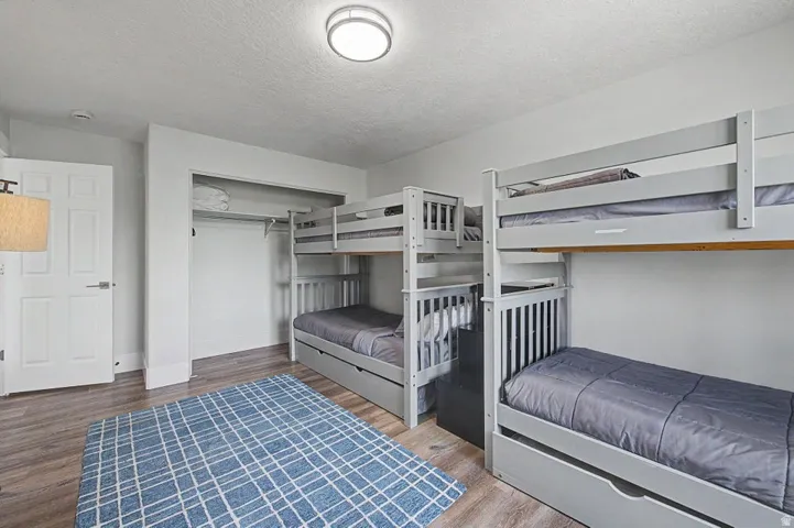Room featuring two sets of bunk beds with built-in storage drawers, wood-finish flooring, a flush-mount ceiling light, and a white paneled door