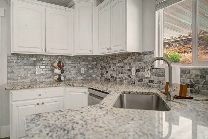 Kitchen featuring white cabinetry, speckled countertops, a mosaic tile backsplash, a stainless steel undermount sink, and a gooseneck faucet