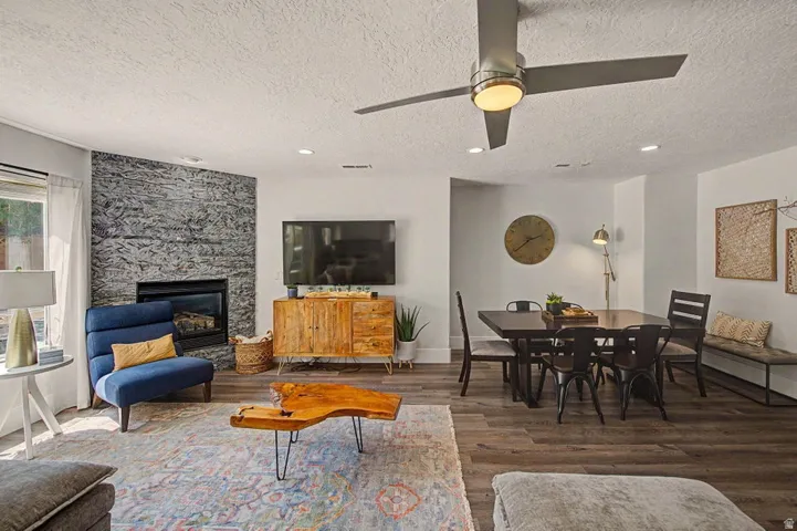 Living area featuring a floor-to-ceiling stone fireplace, ceiling fan with integrated lighting, recessed lighting, wood-finish flooring, and a large window with sheer drapes