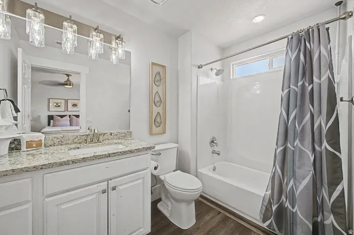 Bathroom featuring a white vanity with a light-toned countertop, a shower-tub combination, wood-finish flooring, and a window above the tub