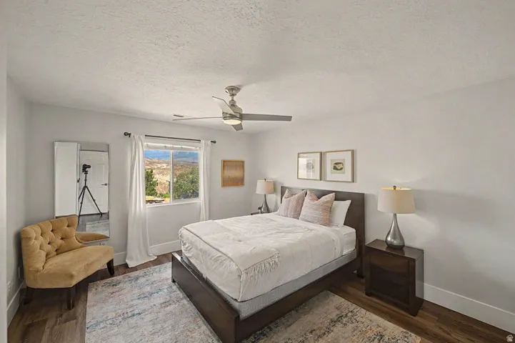Bedroom featuring wood-finish flooring, a ceiling fan with integrated lighting, a window with outdoor scenery, and neutral wall tones
