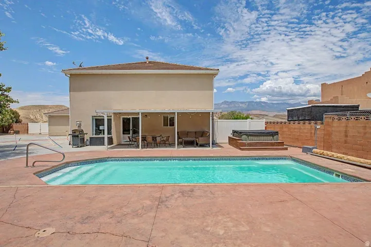 Backyard oasis featuring an in-ground swimming pool, stamped concrete patio, covered patio area, raised hot tub platform, and mountain backdrop