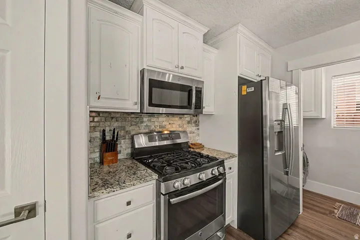 Kitchen featuring stainless steel appliances, white cabinetry, a mosaic tile backsplash, and granite countertops