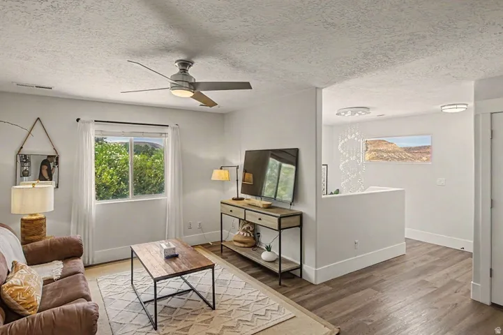 Bright and open living space featuring wood-finish flooring, a ceiling fan with integrated lighting, and large glass doors allowing natural light