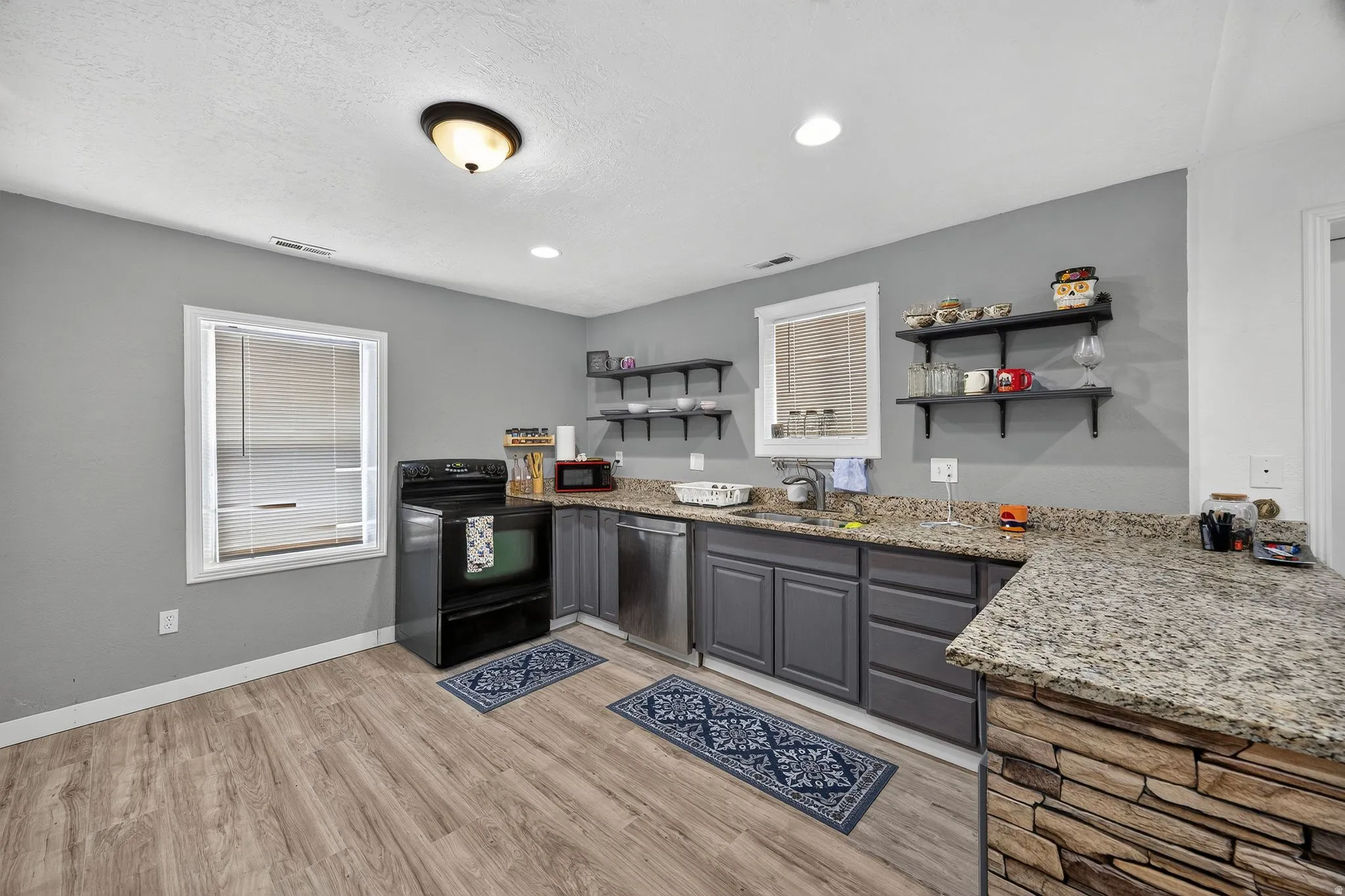 Kitchen featuring stone-finish countertops, wood-finish flooring, dark cabinetry, and stainless steel appliances