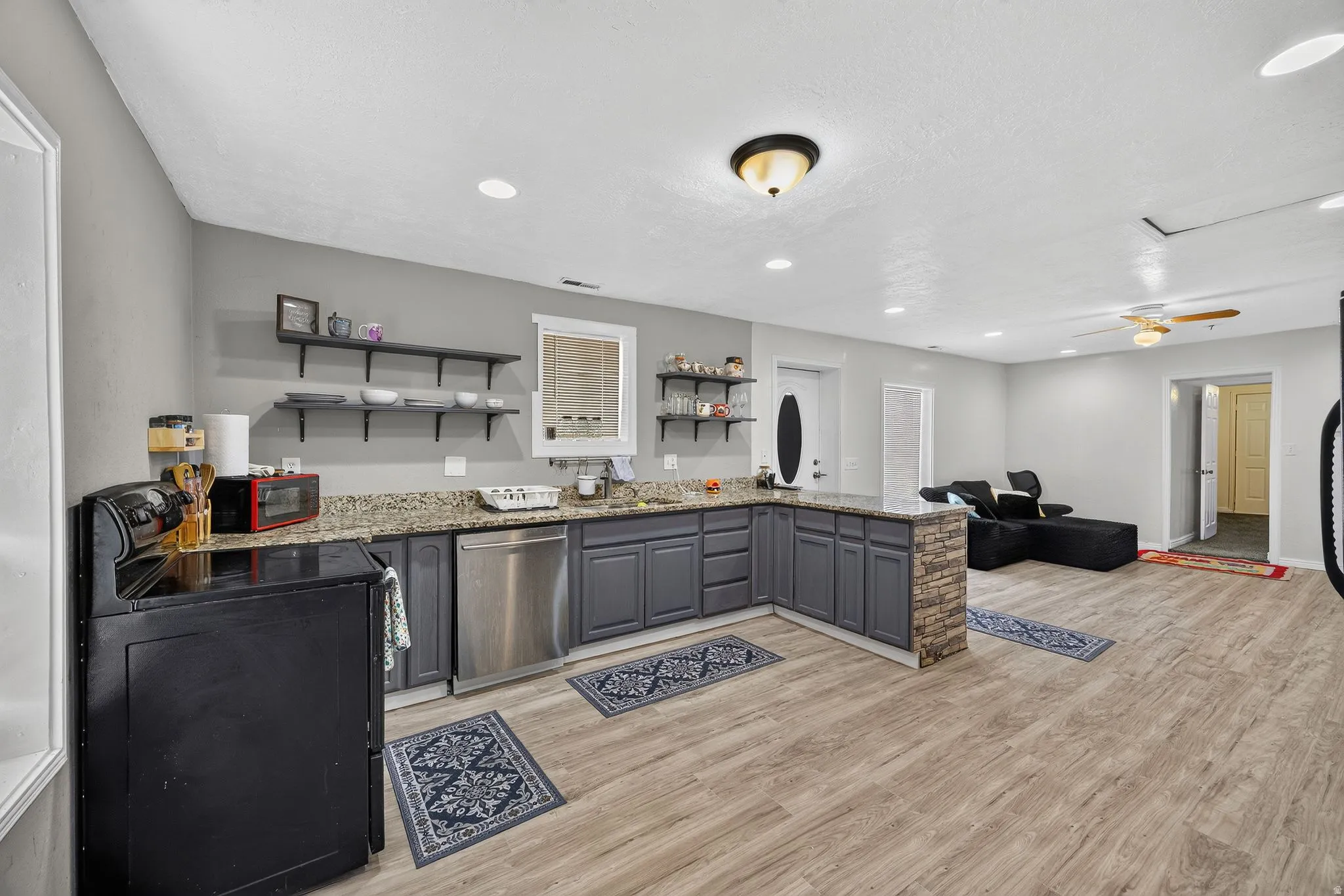 Kitchen featuring wood-finish flooring, dark grey cabinetry, granite-style countertops, stainless steel appliances, and recessed lighting