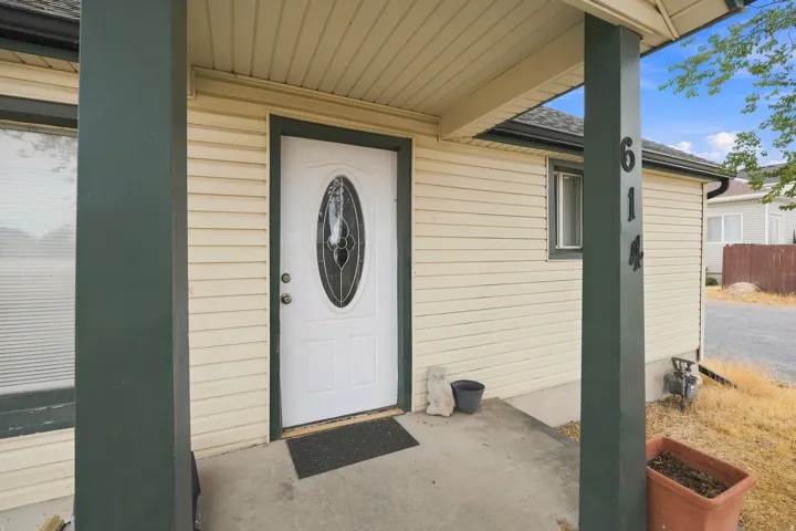 Covered front porch entry featuring a white oval-lite door with decorative glass, beige horizontal siding, dark green trim, and a concrete pathway