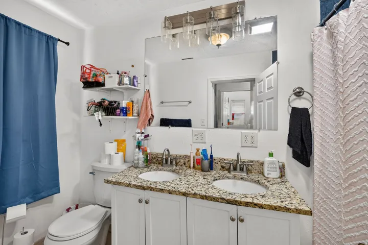 Bathroom featuring a dual vanity with a granite-style countertop, white cabinetry, and two undermount sinks