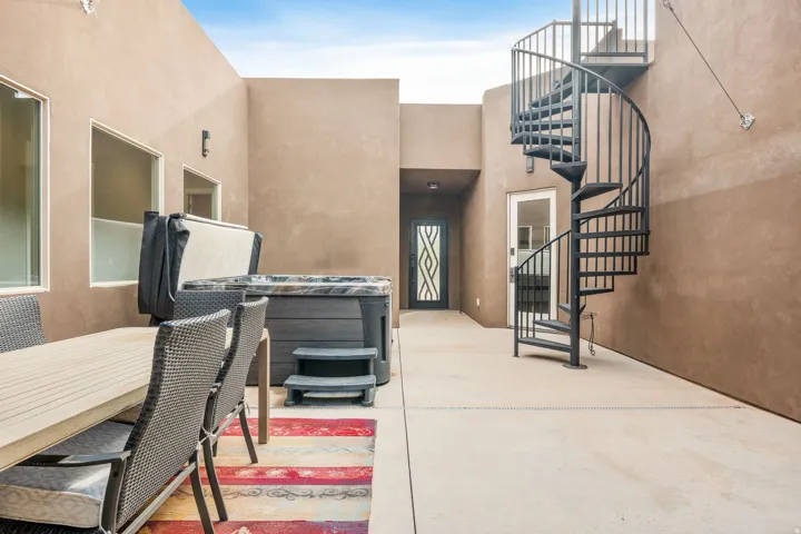 Expansive outdoor patio featuring a hot tub, a black spiral staircase, and a decorative frosted glass entry door