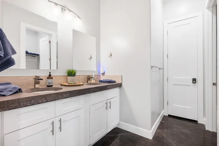 Dual vanity with integrated sinks, white shaker cabinetry, dark countertop, brushed nickel fixtures, and a modern light bar