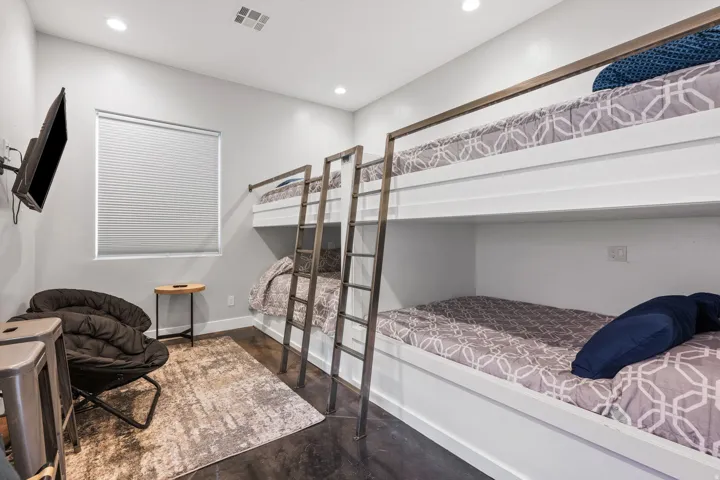Room featuring built-in bunk beds with metal ladders and railings, recessed lighting, a single window with blinds, and dark concrete flooring