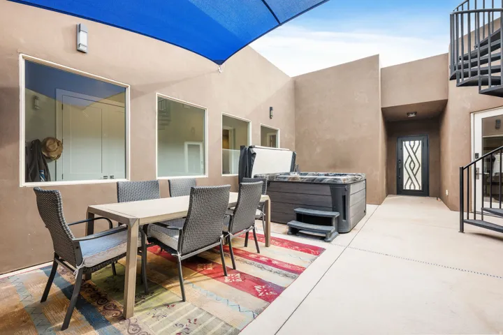 Private outdoor patio featuring a hot tub, a stylish shade sail, and a black wrought iron spiral staircase