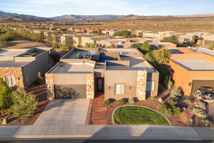 Contemporary stucco and stone exterior featuring a flat roofline, integrated garage, concrete driveway, and front yard landscaping with decorative rock and a grass area
