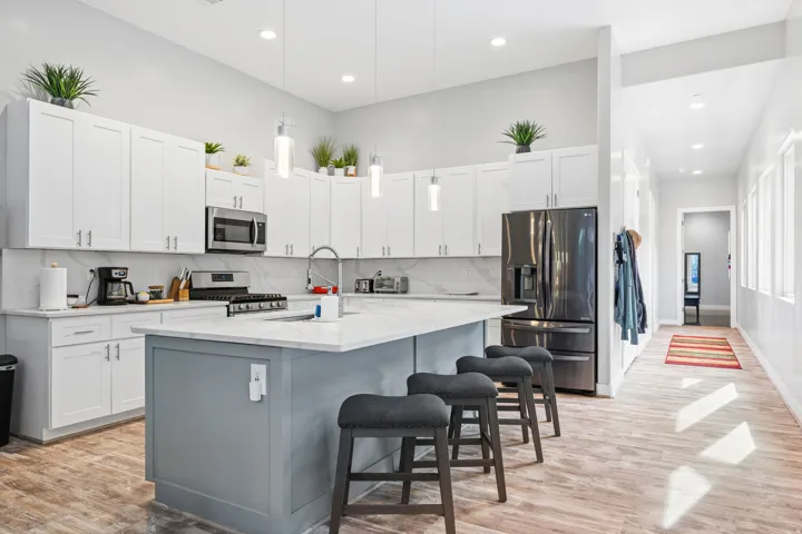 Contemporary kitchen featuring white cabinetry, a large center island with a sink and pendant lighting, stainless steel appliances, and wood-finish flooring