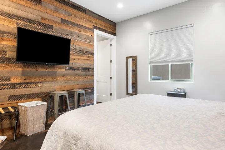 Accent wall with horizontal wood planks, mounted flat-screen television, recessed ceiling lighting, light gray painted walls, and a casement window with blinds
