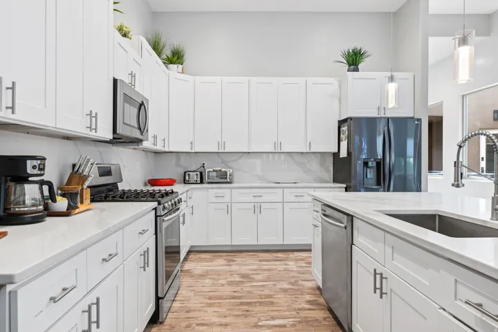 Bright kitchen featuring white shaker cabinetry, stainless steel appliances, light countertops, a coordinating backsplash, and wood-finish flooring