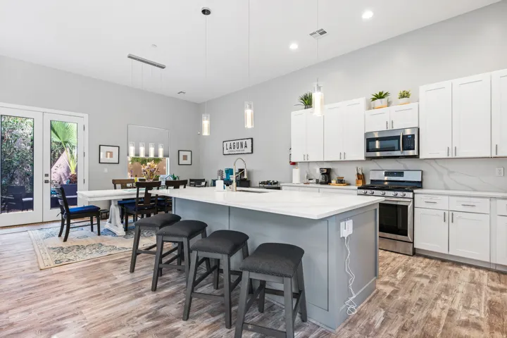 Spacious kitchen featuring an expansive center island with seating, stainless steel appliances, white cabinetry, and wood-finish flooring