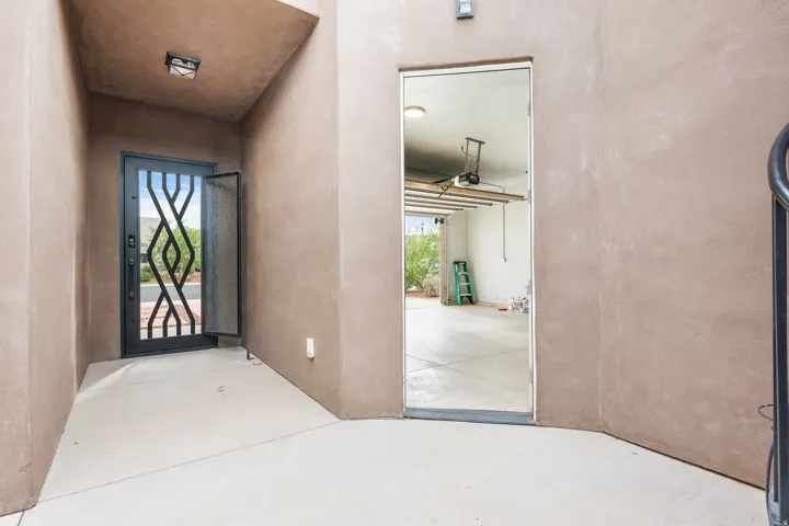 Entryway featuring a decorative wrought iron security door, stucco exterior, concrete flooring, and a flush-mount ceiling light fixture