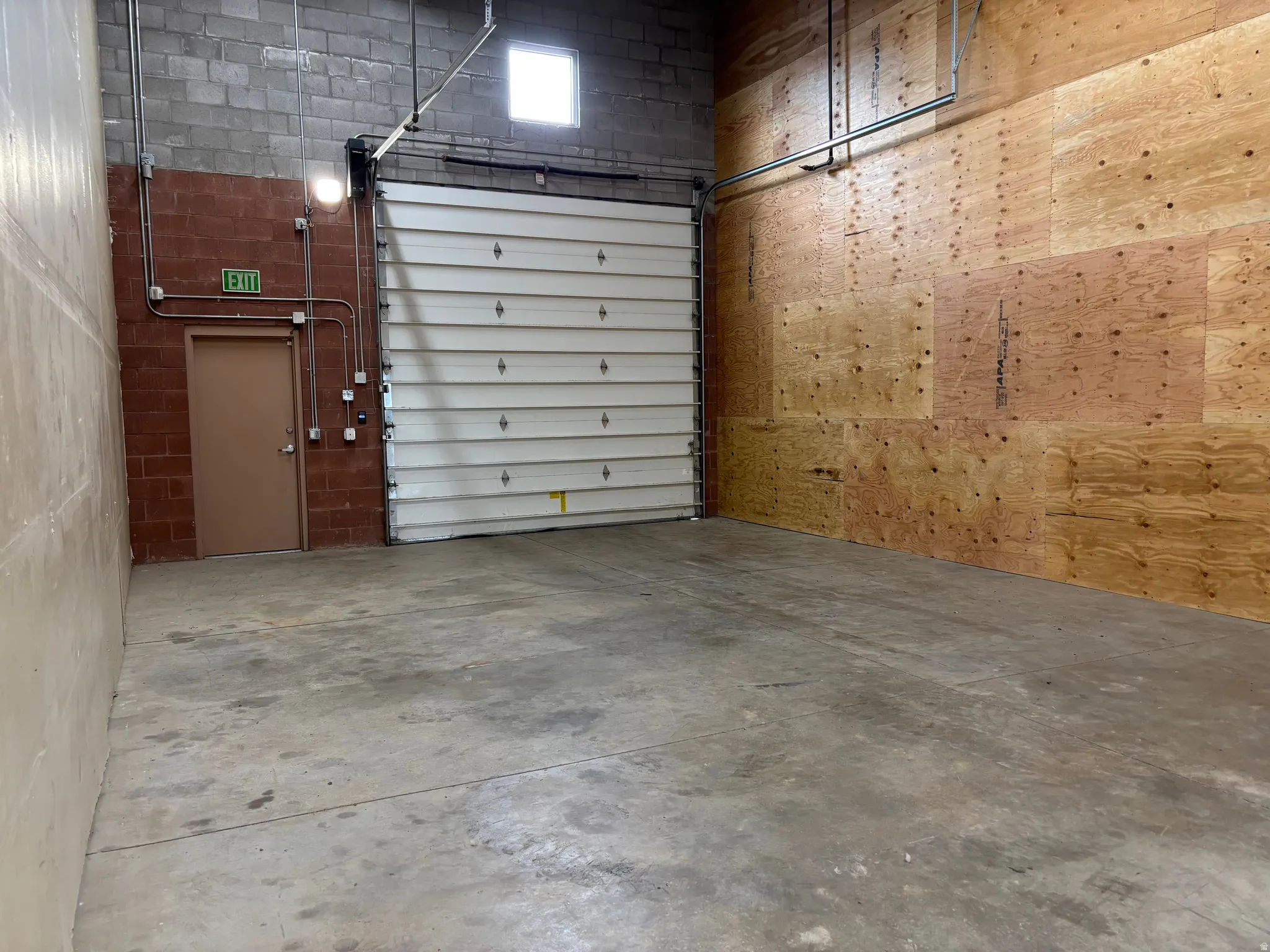 Spacious industrial bay featuring a large roll-up door, concrete flooring, and a separate entry door