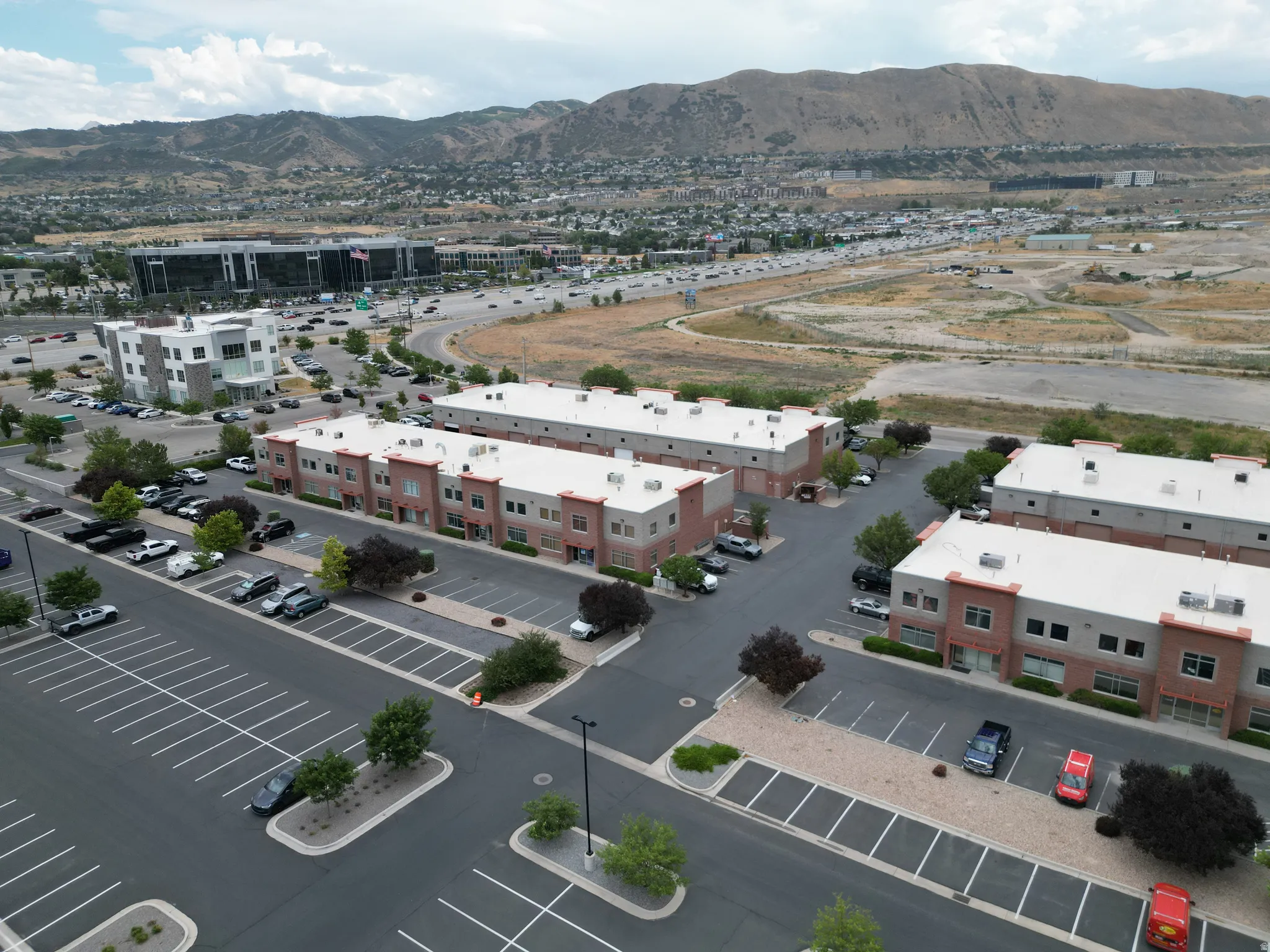 Commercial complex featuring multiple brick and stucco buildings, ample paved parking, and mature landscaping
