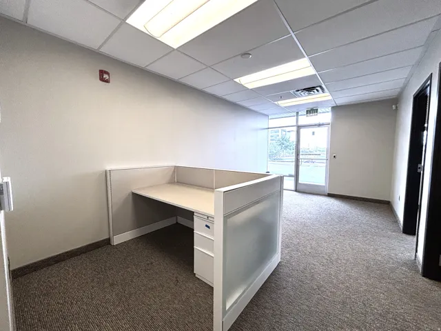 Office space featuring a built-in workstation, carpeted flooring, drop ceiling with fluorescent lighting, and a glass paneled entry door