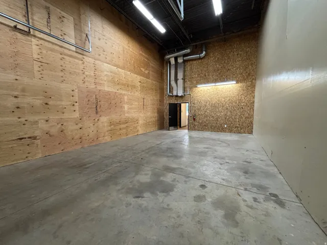 Spacious industrial interior featuring concrete flooring, exposed ceiling with strip lighting, and a blend of plywood and painted walls