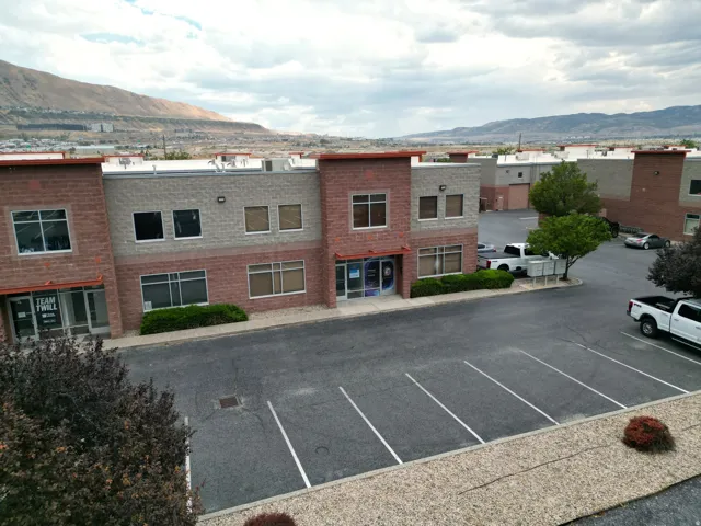 Commercial building featuring a brick and block facade, multiple windows across two levels, and an asphalt parking area with painted lines
