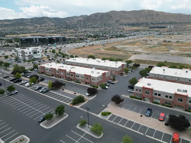 Commercial complex featuring multiple brick and stucco buildings, ample paved parking, and mature landscaping