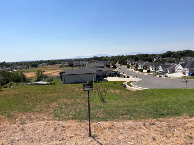 Expansive lot with varied terrain, featuring green and dry grass, a partial residential street, and distant mountain backdrops