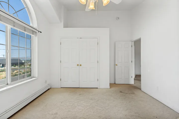 Room featuring a large arched window with horizontal blinds, neutral carpeting, and a ceiling fan with integrated lighting