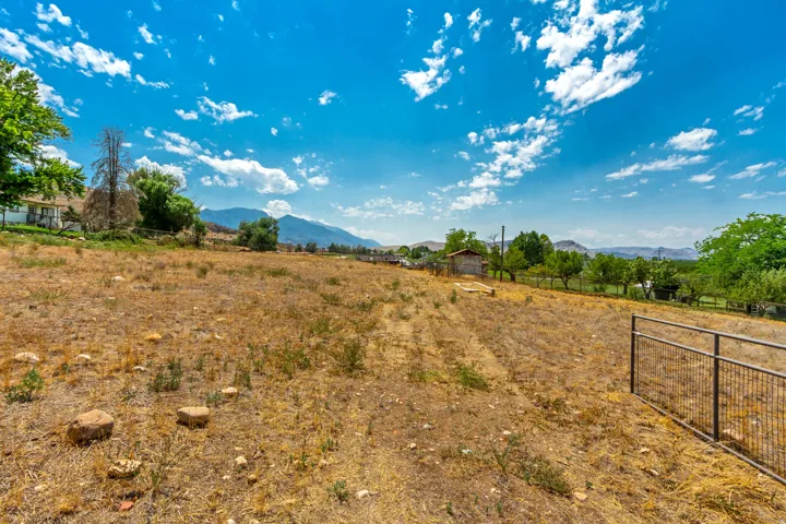 Expansive undeveloped lot featuring a https://assets.utahrealestate.com/photos/280x210/hb5491089_e491b1c6a90dcf198a4ca0dd68af135d_6a6e6474dbdd4.jpgmetal fence, scattered rocks, and distant mountain scenery