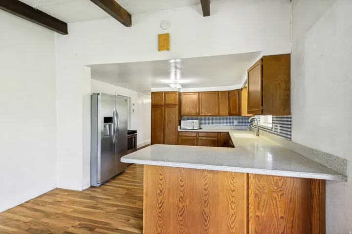 Kitchen featuring wood-finish flooring, exposed ceiling beams, wood cabinetry, light-toned countertops, and a tile backsplash