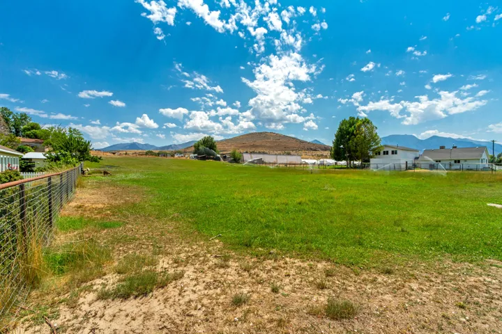Expansive outdoor area featuring a large grassy field, wire fencing, and distant mountain backdrops
